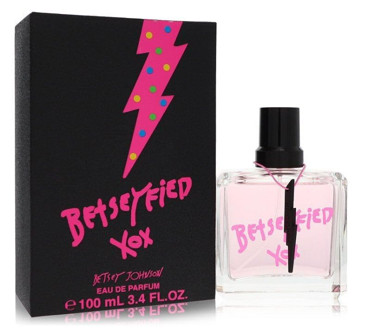 A bottle of Betseyfied by Betsey Johnson Eau De Parfum, Fragrance for Women is placed next to its black box. The box is adorned with a pink and colorful polka-dotted lightning bolt and pink text. Inside the bottle is a light pink liquid, topped with a pink cap.