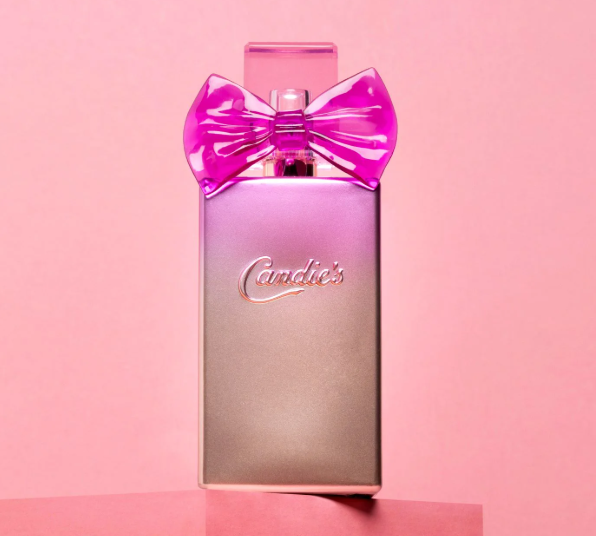 A stylish bottle of Candie's Charm Fragrance, adorned with a glossy pink bow, is set against a pink background. The metallic bottle features the embossed brand name "Candie's" on the front and is elegantly placed on a pink platform.