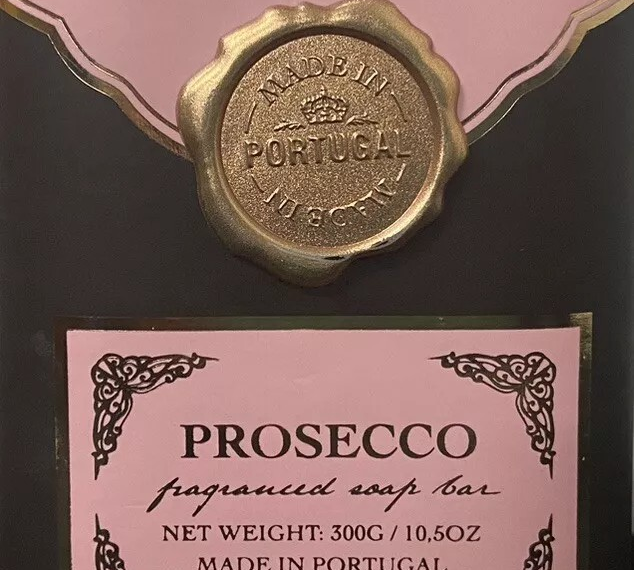 A package of Castelbel Editions Prosecco fragranced soap bars features two 7oz bars with a design that includes a pink and black color scheme, decorative details, and a gold wax seal. The label indicates it is made in Portugal.